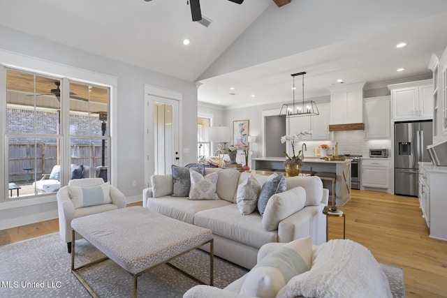 living room with light wood-type flooring, recessed lighting, high vaulted ceiling, and ceiling fan with notable chandelier