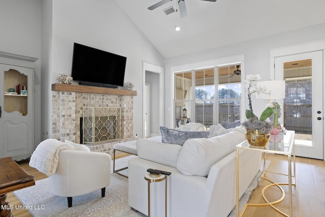 living area featuring visible vents, a ceiling fan, a tiled fireplace, light wood-style floors, and high vaulted ceiling