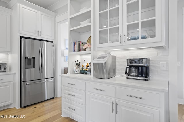 kitchen with tasteful backsplash, light countertops, glass insert cabinets, white cabinets, and stainless steel fridge