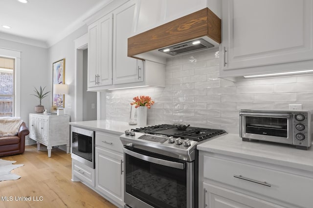 kitchen with stainless steel gas range oven, a toaster, white cabinets, light countertops, and premium range hood