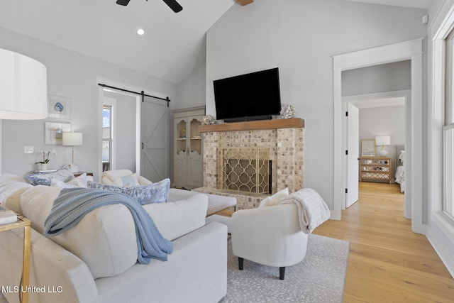 living area with a barn door, a ceiling fan, light wood-type flooring, high vaulted ceiling, and recessed lighting