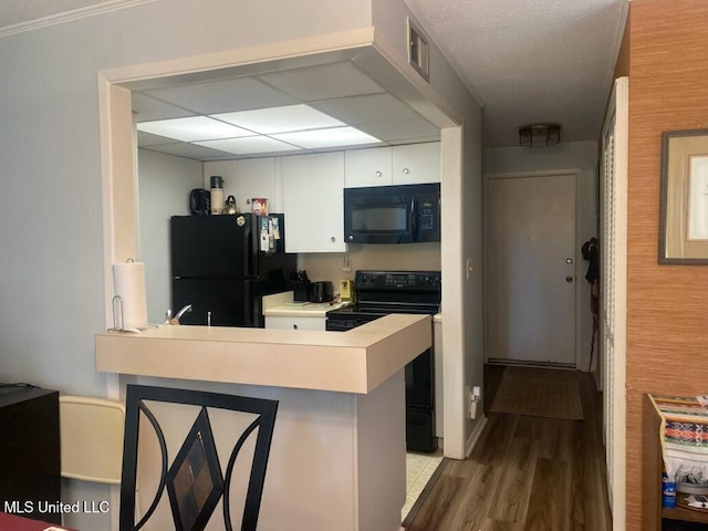 kitchen featuring a peninsula, wood finished floors, visible vents, white cabinets, and black appliances