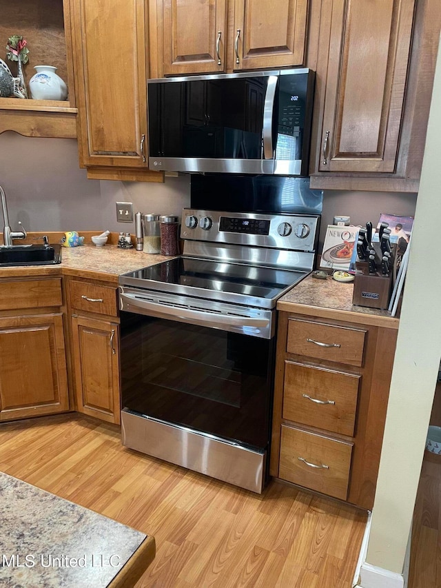 kitchen featuring light stone counters, appliances with stainless steel finishes, sink, and light wood-type flooring