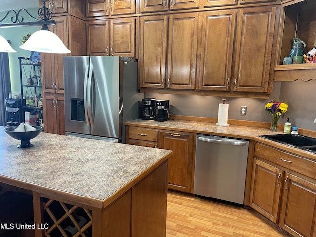 kitchen with a kitchen island, light hardwood / wood-style flooring, hanging light fixtures, stainless steel appliances, and sink