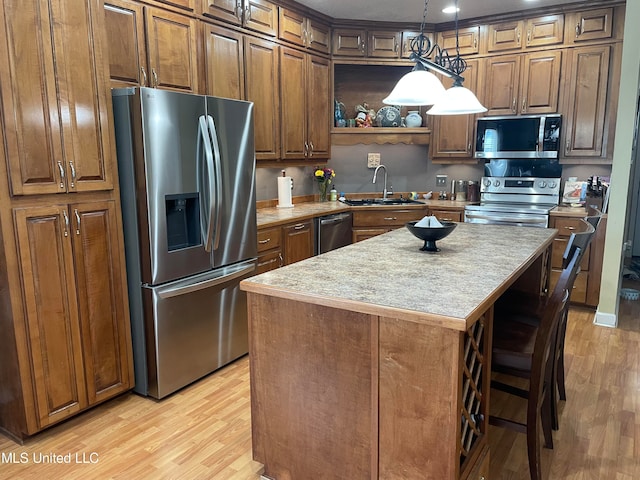 kitchen featuring hanging light fixtures, light wood-type flooring, stainless steel appliances, sink, and a center island