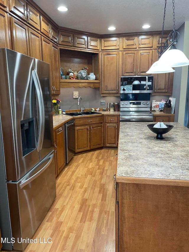 kitchen with sink, appliances with stainless steel finishes, light hardwood / wood-style flooring, and decorative light fixtures