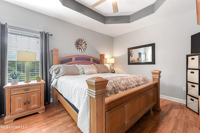 bedroom featuring ceiling fan, a tray ceiling, and light hardwood / wood-style flooring