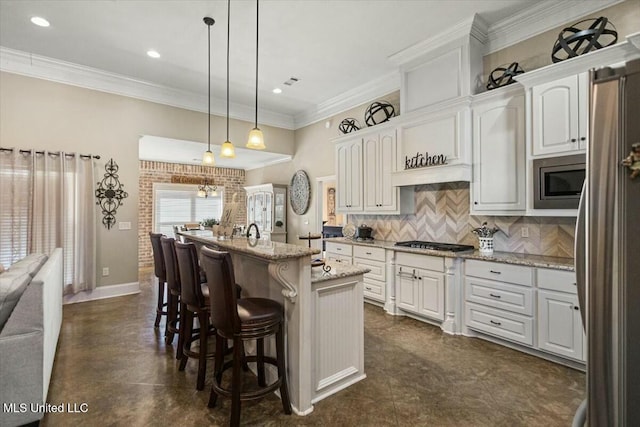 kitchen with light stone counters, a kitchen island with sink, white cabinets, appliances with stainless steel finishes, and backsplash