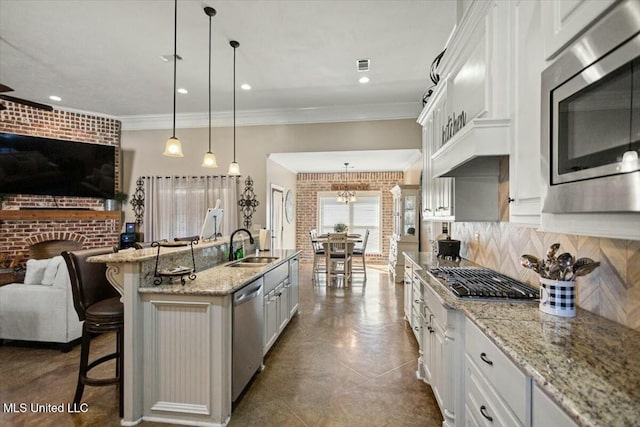 kitchen featuring stainless steel appliances, brick wall, a sink, open floor plan, and a kitchen bar