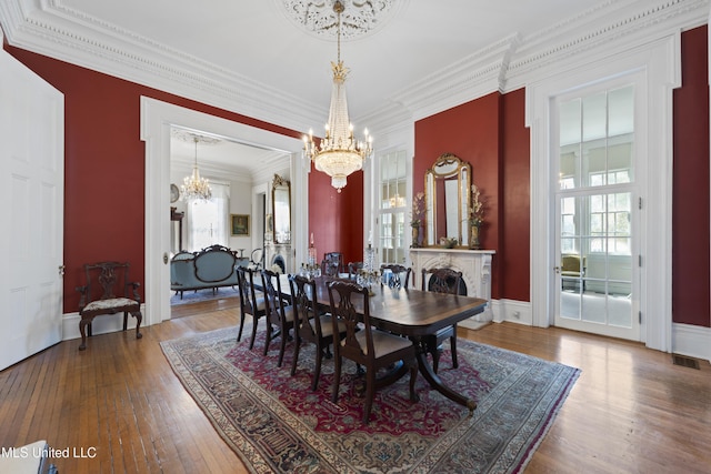 dining room featuring visible vents, baseboards, hardwood / wood-style floors, an inviting chandelier, and crown molding