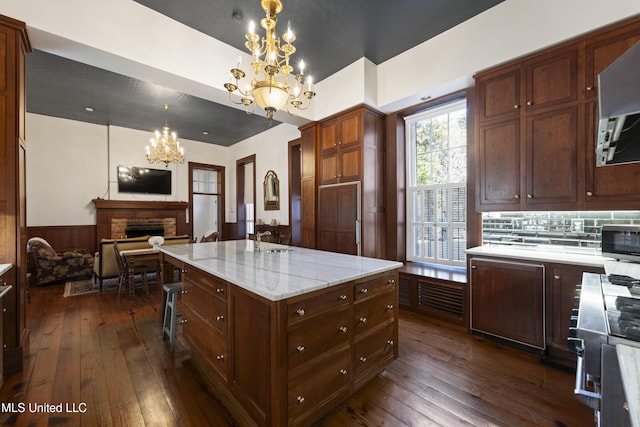 kitchen featuring dark wood-style floors, a wainscoted wall, a fireplace, and an inviting chandelier