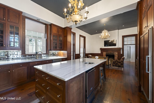 kitchen featuring a fireplace, an inviting chandelier, open floor plan, a kitchen island with sink, and a sink