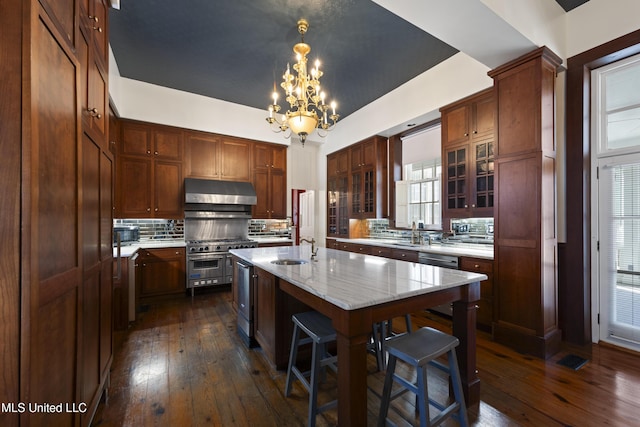 kitchen featuring dark wood finished floors, stainless steel appliances, a sink, an island with sink, and under cabinet range hood