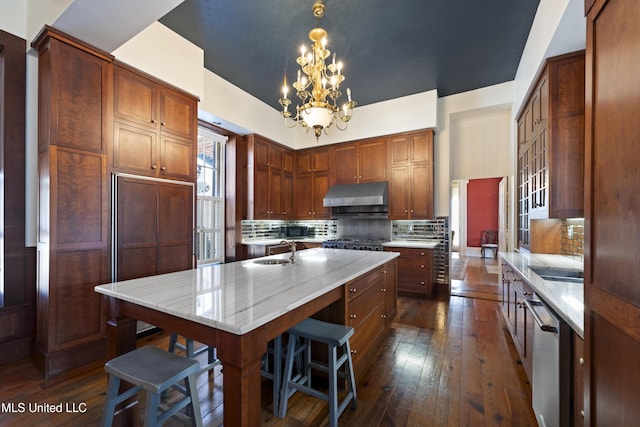 kitchen featuring dark wood finished floors, backsplash, a sink, and under cabinet range hood