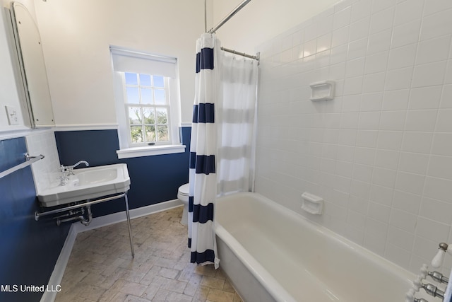 bathroom with toilet, shower / bathtub combination with curtain, baseboards, and a sink