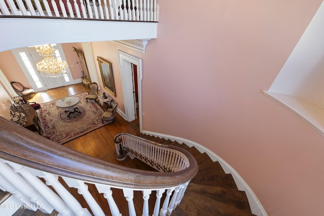 stairway with baseboards, a high ceiling, wood finished floors, and a notable chandelier