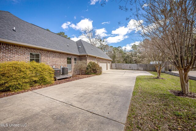 view of property exterior with driveway, cooling unit, roof with shingles, a garage, and brick siding