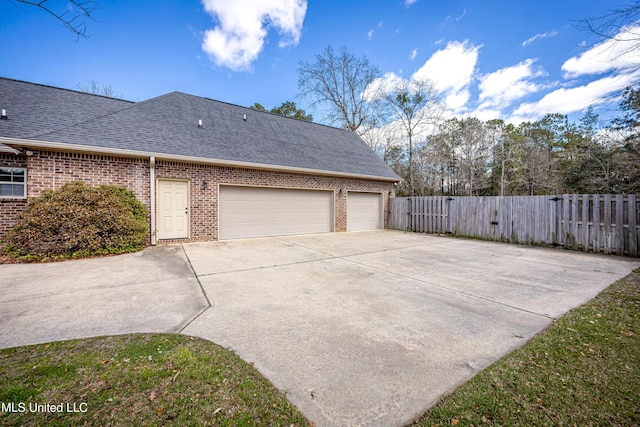 view of side of property with brick siding, a shingled roof, fence, concrete driveway, and a garage