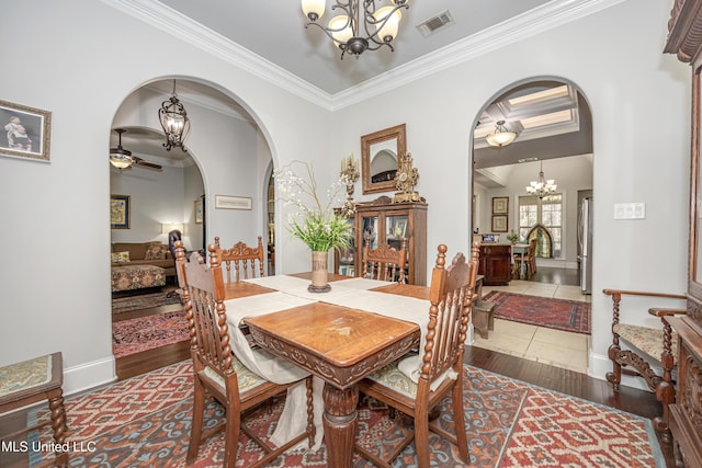 dining room featuring wood finished floors, visible vents, arched walkways, crown molding, and ceiling fan with notable chandelier