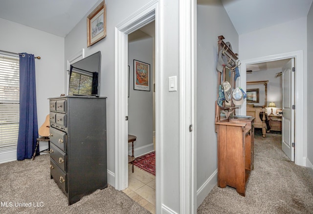 corridor featuring light tile patterned floors, baseboards, and light carpet