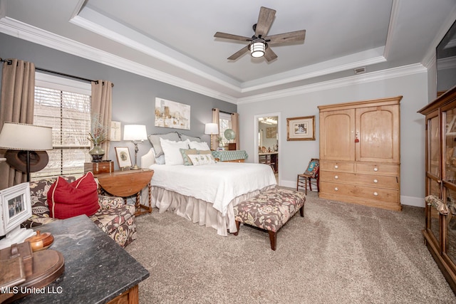 carpeted bedroom featuring baseboards, ensuite bath, a tray ceiling, ceiling fan, and crown molding