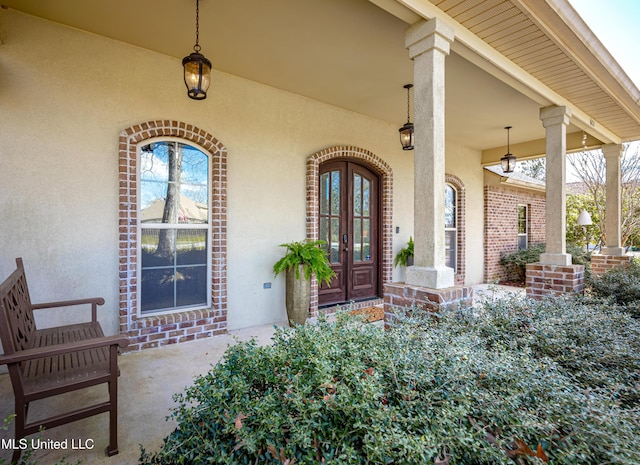 view of exterior entry with french doors, brick siding, and stucco siding