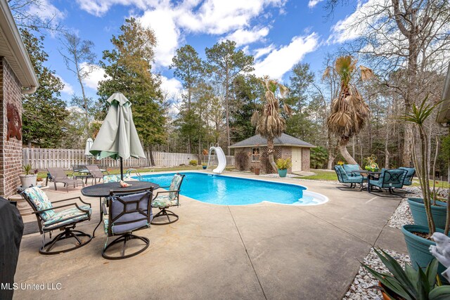 view of swimming pool featuring a fenced in pool, a water slide, a fenced backyard, an outbuilding, and a patio