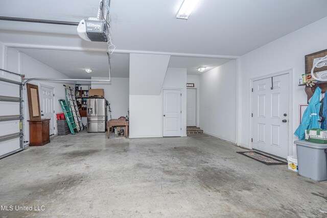 garage with stainless steel fridge and a garage door opener