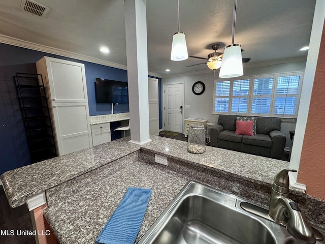 kitchen with sink, crown molding, hanging light fixtures, dark stone countertops, and white cabinetry