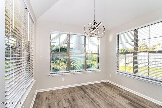 spare room with a chandelier, hardwood / wood-style floors, vaulted ceiling, and a healthy amount of sunlight