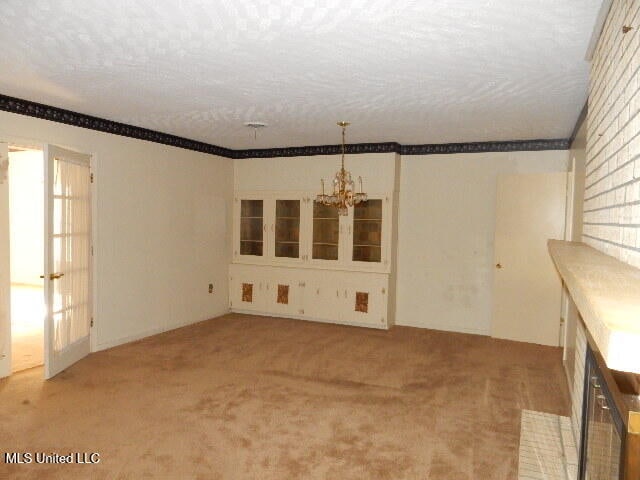 unfurnished room featuring a notable chandelier, a textured ceiling, and light colored carpet