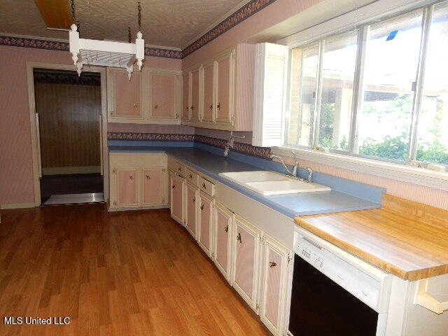 kitchen featuring white dishwasher, sink, pendant lighting, white cabinets, and light hardwood / wood-style floors