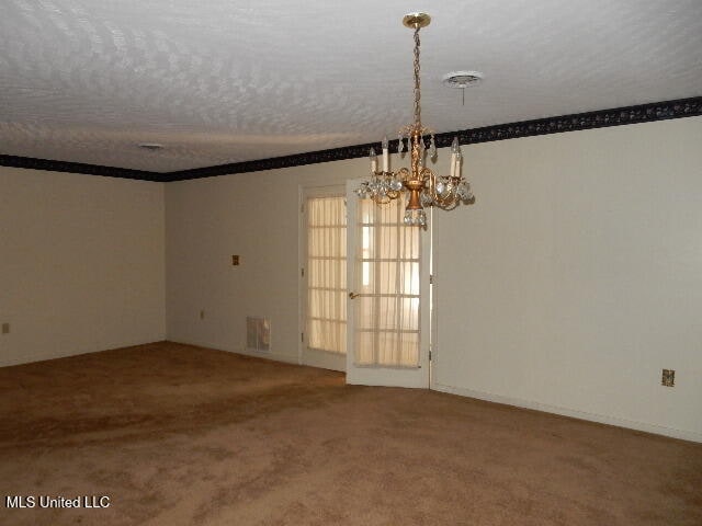 carpeted spare room featuring a textured ceiling and an inviting chandelier