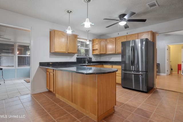 kitchen featuring kitchen peninsula, stainless steel fridge, hanging light fixtures, light tile patterned flooring, and sink