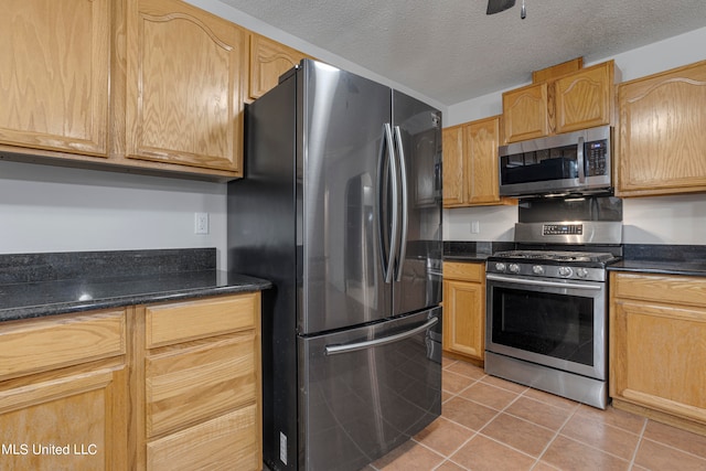 kitchen featuring appliances with stainless steel finishes, a textured ceiling, dark stone countertops, and light tile patterned floors