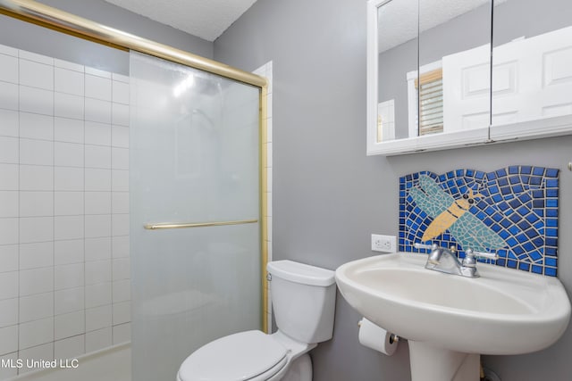 bathroom featuring toilet, an enclosed shower, a textured ceiling, and sink