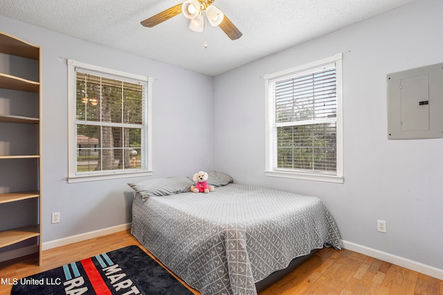 bedroom featuring ceiling fan, multiple windows, electric panel, and hardwood / wood-style floors