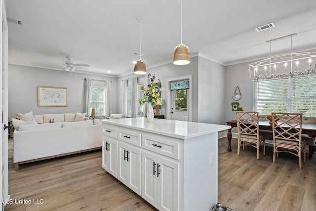 kitchen with white cabinets, light wood-type flooring, ceiling fan with notable chandelier, decorative light fixtures, and a center island