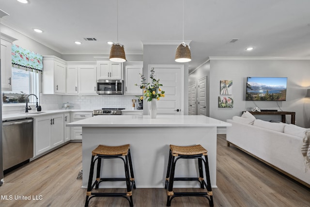 kitchen featuring white cabinetry, light hardwood / wood-style floors, stainless steel appliances, and decorative light fixtures