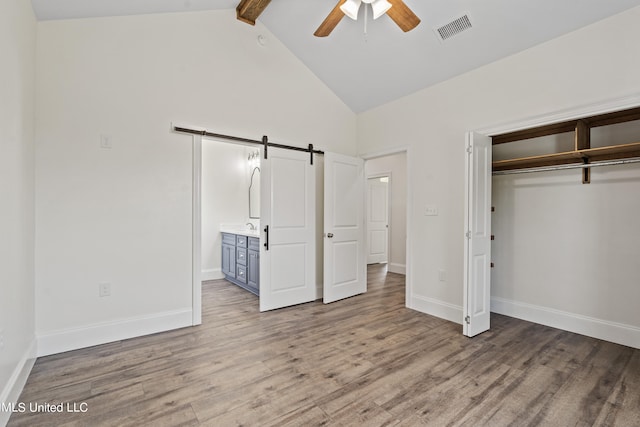 unfurnished bedroom with a closet, light hardwood / wood-style flooring, a barn door, and ceiling fan