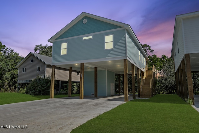 back house at dusk featuring a lawn and a carport