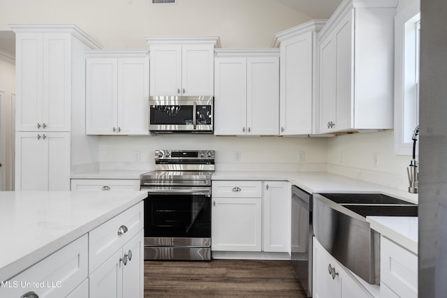 kitchen featuring appliances with stainless steel finishes, white cabinets, light stone counters, and dark wood-type flooring