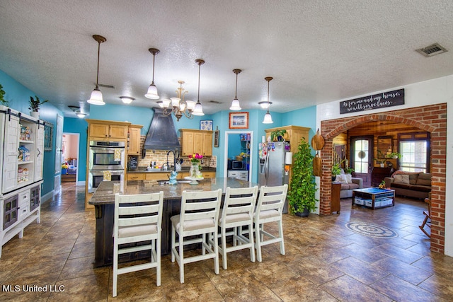 kitchen featuring stainless steel appliances, decorative backsplash, hanging light fixtures, a textured ceiling, and a kitchen breakfast bar