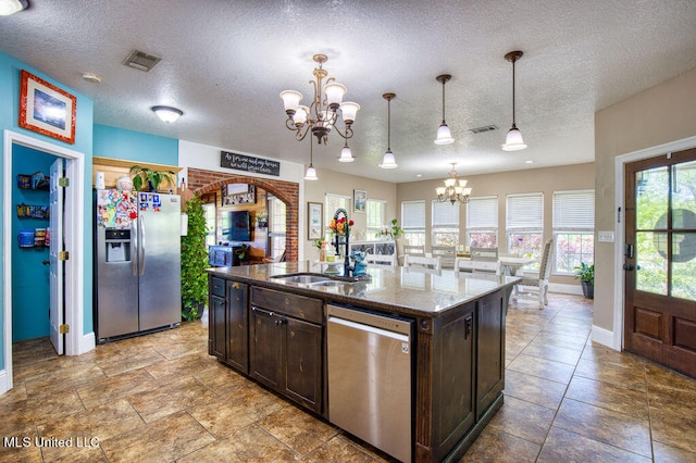 kitchen with stainless steel appliances, hanging light fixtures, a textured ceiling, and an island with sink