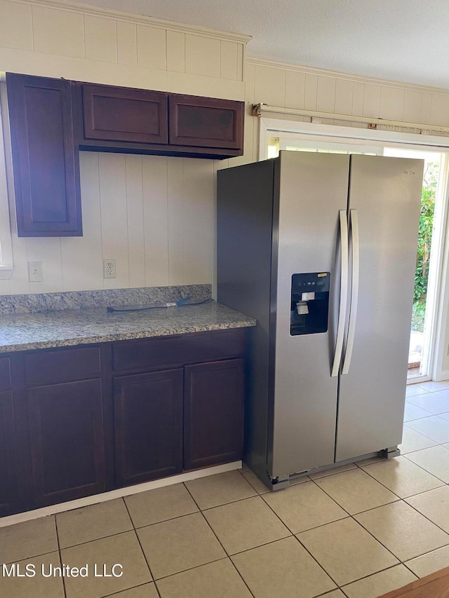 kitchen with blue cabinetry, a textured ceiling, stainless steel fridge with ice dispenser, light stone counters, and light tile patterned floors