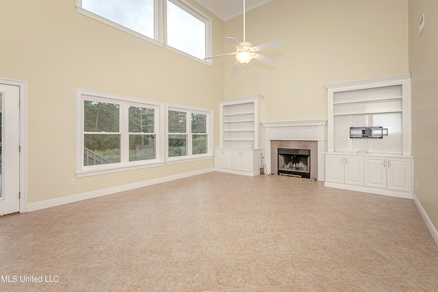 unfurnished living room with a wealth of natural light, built in features, a towering ceiling, and ceiling fan