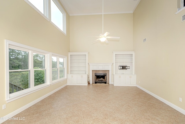 unfurnished living room with crown molding, a towering ceiling, built in shelves, and ceiling fan