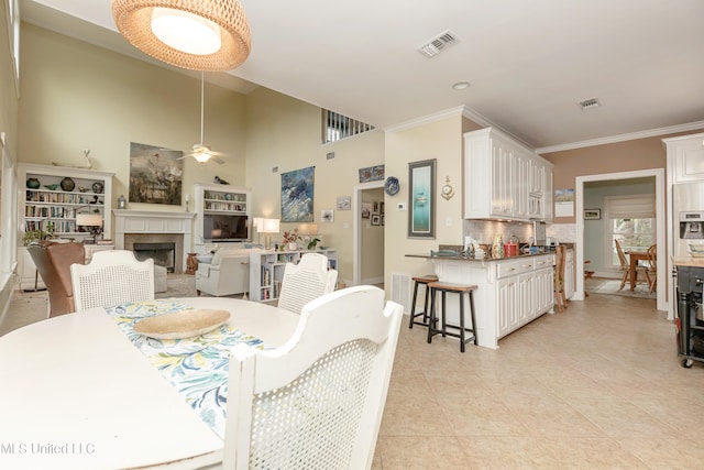 tiled dining space featuring ceiling fan, crown molding, and a fireplace