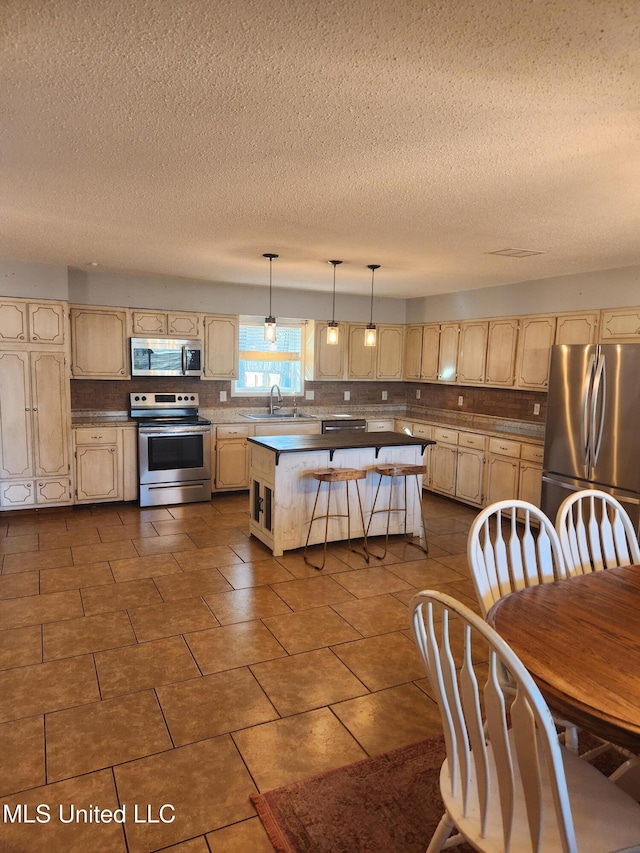 kitchen with a kitchen island, appliances with stainless steel finishes, sink, hanging light fixtures, and a textured ceiling