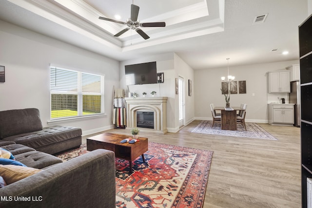7380 Shearwater Way, Ocean Springs, MS 39564 - living room with a raised ceiling, light wood-style floors, a glass covered fireplace, a ceiling fan, and a chandelier